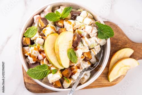 Tasty Taffy Apple Salad with fresh ripe apples, marshmallows, caramel peanut candy bars, nuts, cool whip and caramel sauce topping, tasty and sweet traditional american fruit dessert