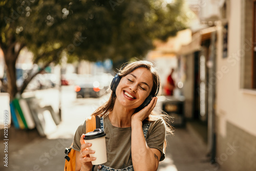 Happy young woman enjoying music walking city street