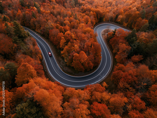 Aerial top view of winding road in vibrant autumn forest with red car 