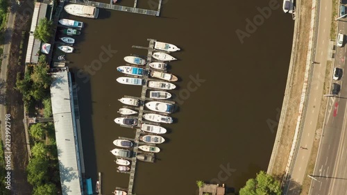 Motorboats and luxury yachts dock at a river marina along an urban embankment. The nautical pier offers boat rental and harbor parking for summer leisure and water transportation services.