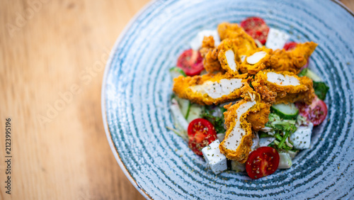 A fresh salad in a bowl, with chicken, cherry tomatoes, cucumbers and cheese.