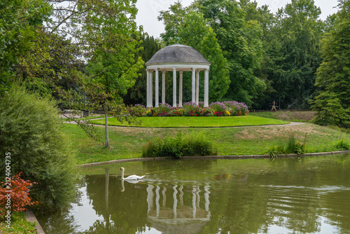 White pavilion in a blooming garden with a pond and a swan in the water. a round, shaded shelter in the Parc de l'Orangerie in Strasbourg.