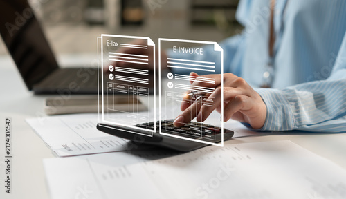 Fotografie Businesswoman managing e-tax and e-invoice documents with calculator, laptop and financial paperwork, showcasing digital accounting, tax compliance, electronic billing and modern office workflow