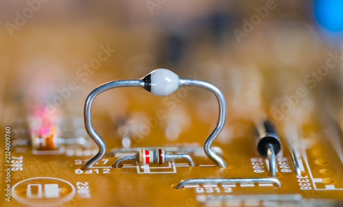 Closeup ultrafast avalanche rectifier diode and color coded resistor on beige PCB. High mounted two-terminal electronic component on orange blur background of printed circuit board. Through-hole tech.