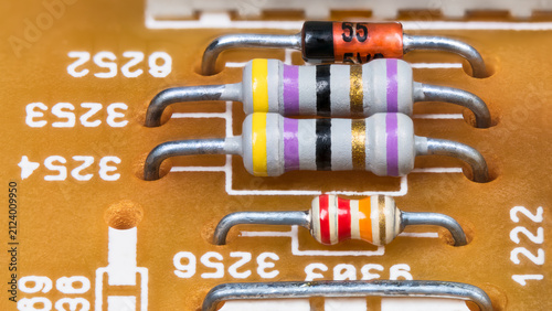White resistors with standard color code, diode and wire jumper on yellow printed circuit board. Closeup of colorful striped electronic components in PCB with through-hole technology. Electrotechnics.