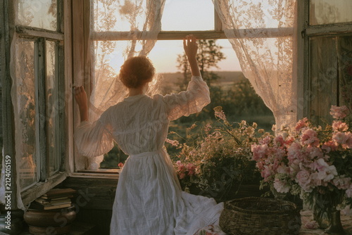 Woman opening vintage windows to a blooming garden at sunrise, capturing peaceful cottage life, spring flowers, fresh air and slow living inspiration.