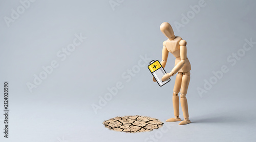 Energy depletion heat anomaly and climate risk management concept with wooden figure holding low battery over cracked earth with copy space for presentation