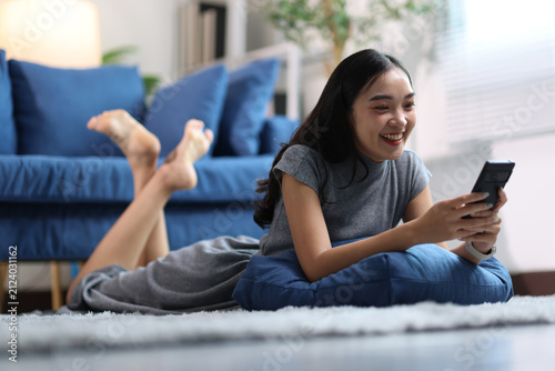 Asian woman relaxing at home using smartphone.