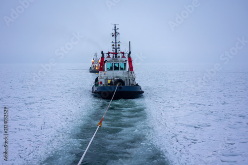 Tugboat Towing Rope Through Ice-Covered Frozen Sea, Maritime Winter Icebreaking Operation. Winter Maritime Logistics and Navigation in Frozen Cold Water, Marine Transportation