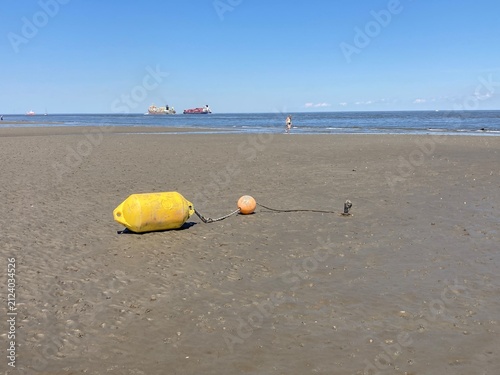 Markierungsbojen liegen trocken im Watt der Nordsee vor Cuxhaven mit Schifffahrtsweg im Hintergrund