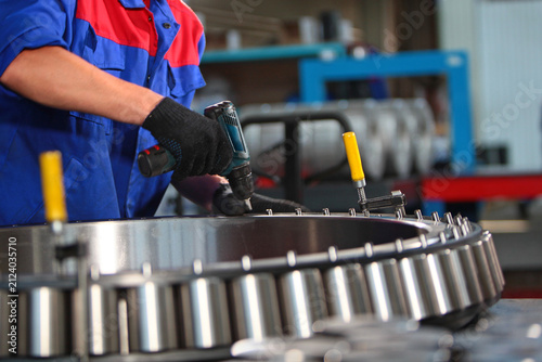Assembly of a large-sized bearing. Close-up of the industrial bearing assembly process at the factory. A cordless screwdriver in the worker's hand. Heavy industry concept