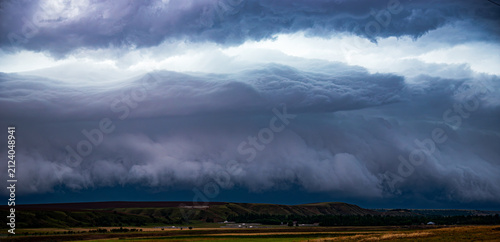 Konstfotografi Dramatic landscape featuring a massive shelf cloud of a supercell thunderstorm moving over a rural road and countryside fields, capturing the powerful atmosphere of an approaching storm