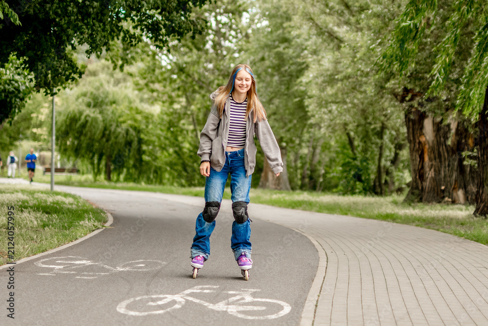 Fototapeta premium Young girl with blonde hair inline skates on a paved park path during daytime.