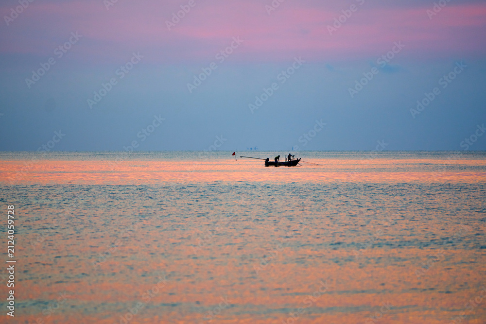 Fototapeta premium Small fishing boat floating on calm ocean water during a vivid colorful sunset horizon.