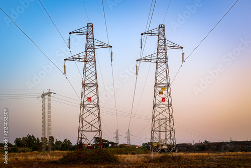 Two high voltage power pylons in a rural field at sunset.