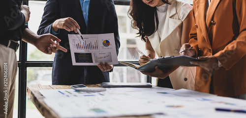 Business people collaborating on strategy, discussing financial charts and data analysis on documents, teamwork in an office.