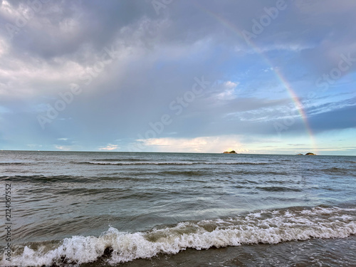 Beautiful rainbow over the ocean waves crashing on the beach under a dramatic sky.