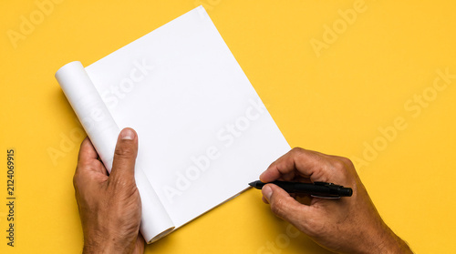 Person holding a rolled white paper sheet and writing with a pen on a yellow background