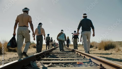 Group of migrant men walking along railway tracks in dry landscape, low angle view, real time