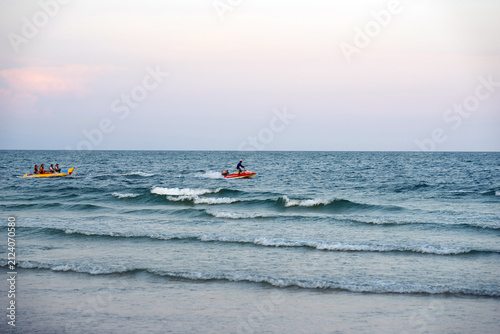 Scenic view of a calm ocean at sunset with small recreational boats or jet skis floating on the gentle waves.