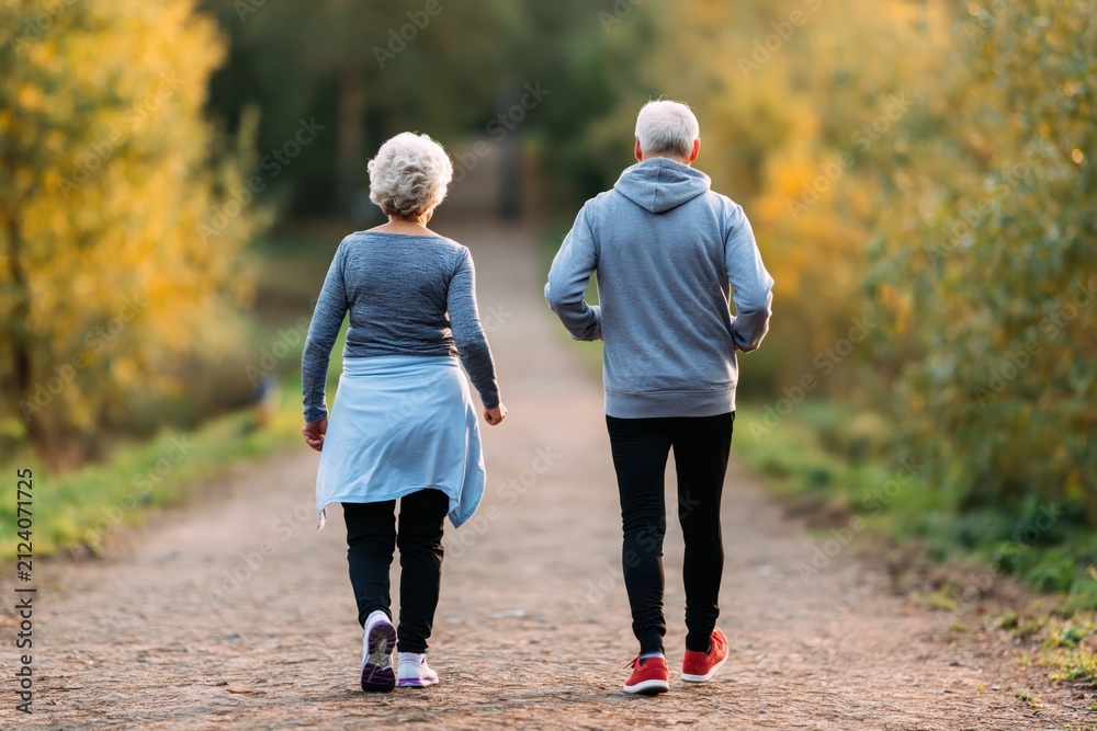 Obraz premium Senior couple walking on a park path for active fitness and a healthy autumn life