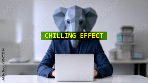 Person in a blue suit wearing a low-poly elephant mask typing on a laptop with text reading CHILLING EFFECT overlaying the face in a bright office environment.