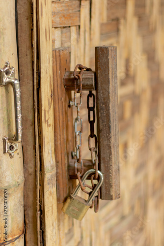 Rusty padlock and chain securing a wooden bamboo door