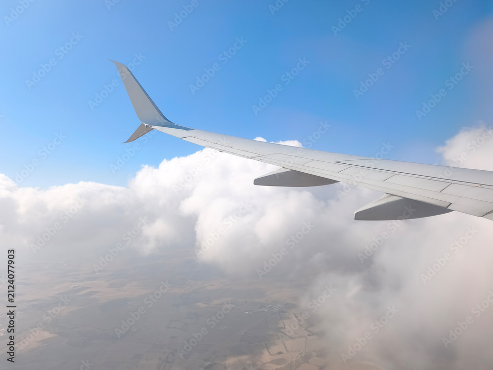 Fototapeta premium View from an Airplane Window with Wing and Clouds. Passenger Window View of Aircraft Wing in the Sky. Scenic Flight View with Airplane Wing and Clouds.