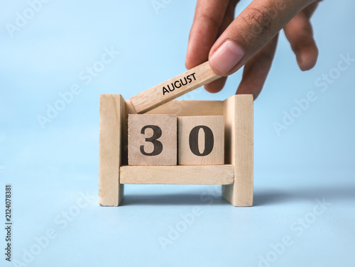Foto A woman's hand holds a wooden block with August written on it on a wooden block calendar for August 30th against a light blue background