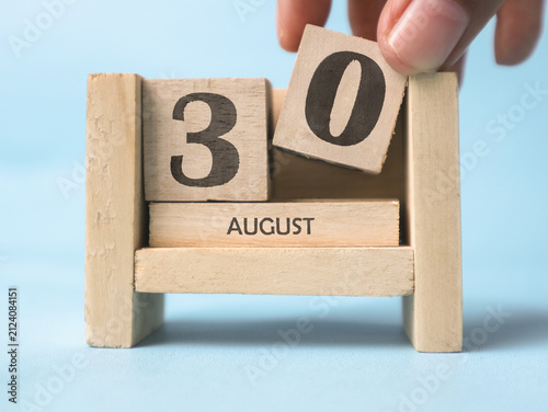 Bild auf Leinwand A woman's hand is holding a wooden block with the number 0 written on it on a wooden block calendar for August 30th on a light blue background