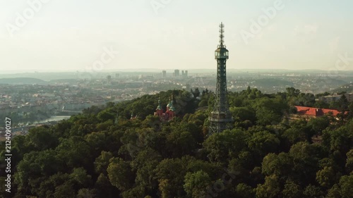 Petrin lookout tower stands in green forest park in early morning Prague. Steel observation structure forms tourist attraction. Historic cityscape represents european travel destination.