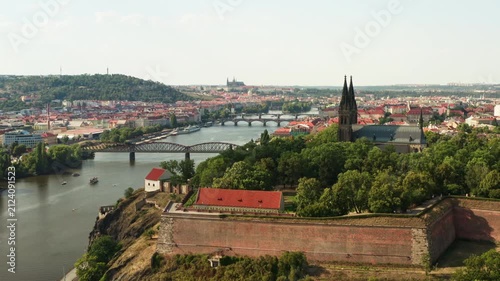 Historic Vysehrad fortress overlooks Vltava river and bridges in Prague. City landmark showcases church spires in scenic urban landscape. Aerial view represents European travel destination.