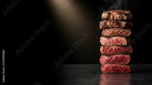 Top view of sliced medium-rare grilled steak with melting butter and rosemary on a dark rustic wooden background