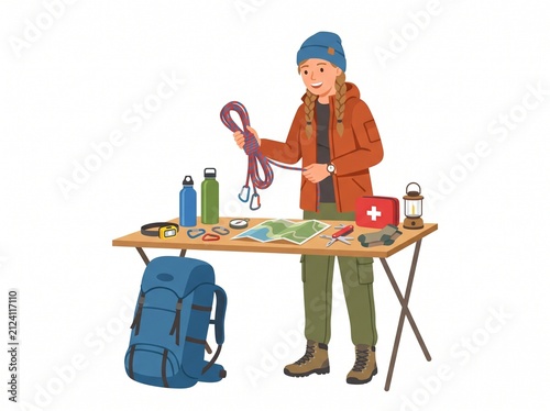 Woman preparing for outdoor adventure with climbing gear and survival equipment laid out on a table
