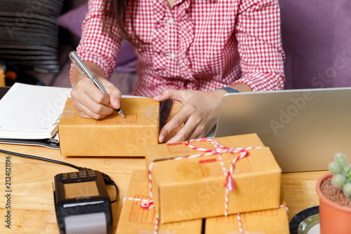 Close up of online seller hand writing address on cardboard box with pen. Small business owner preparing parcel for shipping. E-commerce delivery concept.