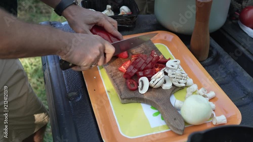 Man slicing fresh red bell pepper and mushrooms outdoors