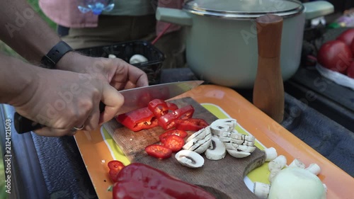 Male hands slicing red pepper and mushrooms outdoors