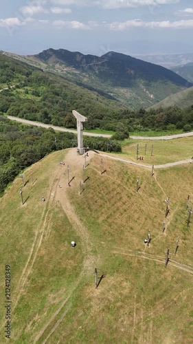 Drone orbiting around the majestic cross monument on mount didgori, revealing the stunning georgian landscape with rolling green hills, lush forests, and a clear blue sky