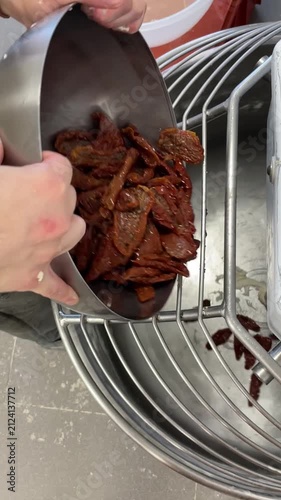 Professional food preparation. Baker adding sun-dried tomatoes from stainless steel bowl into industrial dough mixer. Hands incorporate gourmet ingredients into fresh yeast dough. Vertical UGC