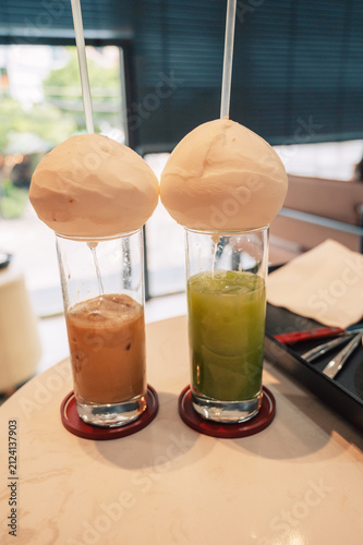 Creative presentation of iced coffee and iced matcha in tall glasses into which coconut water flows from the coconut, served in a modern cafe in Vietnam