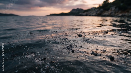 Close-up of rippling dark water surface with small debris reflecting sunset sky over rocky coastline calm ocean background for nature and travel themes