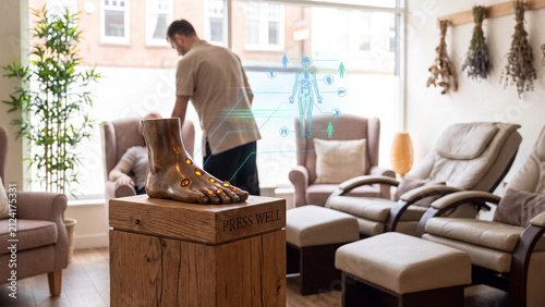 Reflexology foot model displays acupuncture points while a therapist prepares the room for a client session.