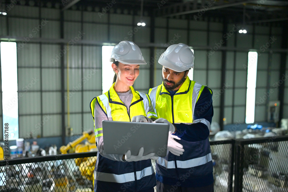 Fototapeta premium Workers discuss plans inside a factory while looking at a laptop during working hours
