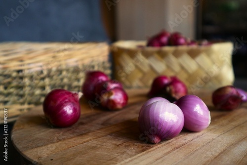 Foto This photo shows several shallot cloves both peeled and unpeeled on a wooden cutting board, as well as a pile of shallots in a woven bamboo basket