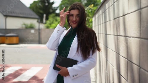 Beautiful young business woman standing near stone wall outdoors with notebook, slow motion