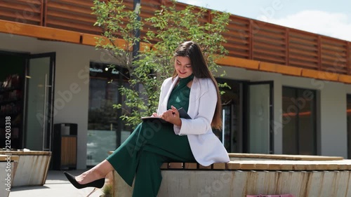 Charming happy businesswoman planning workflow while sitting outside medium shot