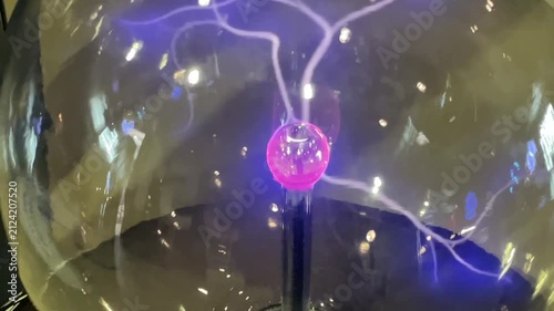 Closeup of transparent plasma ball generating colorful electric discharges that radiate from the center toward the glass surface. Glowing plasma filaments create a dynamic visual effect