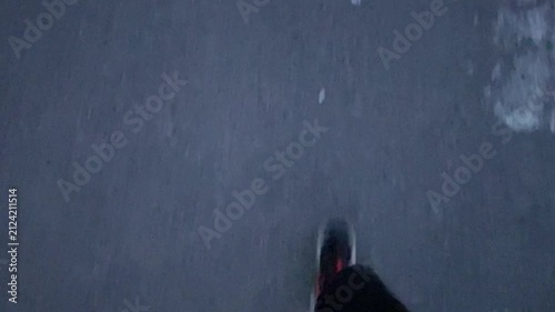POV of a person walking in sneakers across urban concrete pavement during evening hours. The camera looks downward at moving feet.