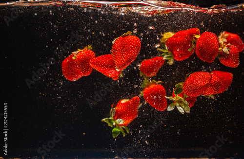 Konstfotografi High speed capture of ripe red strawberries suspended in water with dynamic splashes against a dark background