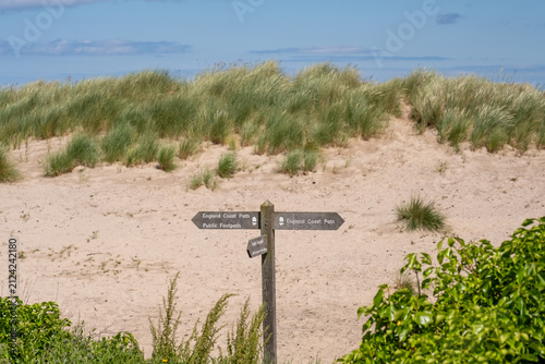 Wooden England Coast Path signpost and way marker in Bamburgh sand dunes, North East coast, guiding walkers along coastal footpath amid grassy dunes.